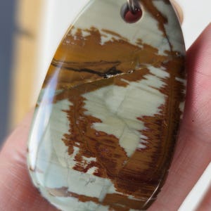 May include: A brown, white, and green oval pendant with a black leather cord. The pendant has a natural stone look with swirls of color.