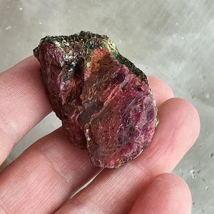 以下が含まれることがあります： 緑色の内包物を含む、粗い赤いルビーの結晶。結晶は約5cmの長さで、自然な研磨されていない表面をしています。