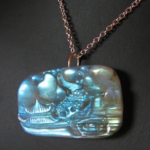 May include: A silver chain necklace with a blue iridescent stone pendant featuring a carved design of a pagoda and trees.