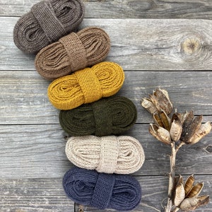 May include: Six spools of different colored cotton rope, arranged vertically on a wooden surface. The colors are brown, tan, yellow, green, beige, and blue.