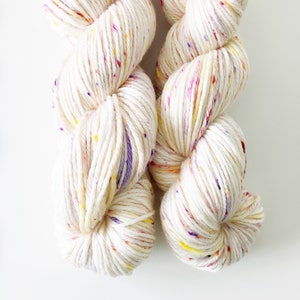 May include: Two skeins of white yarn with colourful flecks. The yarn is soft and fluffy, and it would be perfect for knitting or crocheting.