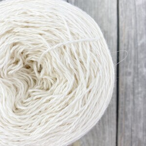 May include: A skein of white yarn, wound into a ball shape, on a wooden surface.