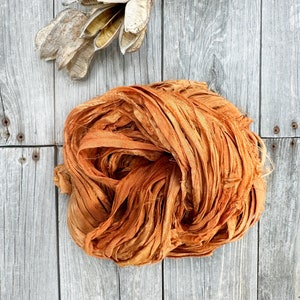 May include: A bundle of orange silk ribbon, loosely tied and arranged on a weathered wooden surface.
