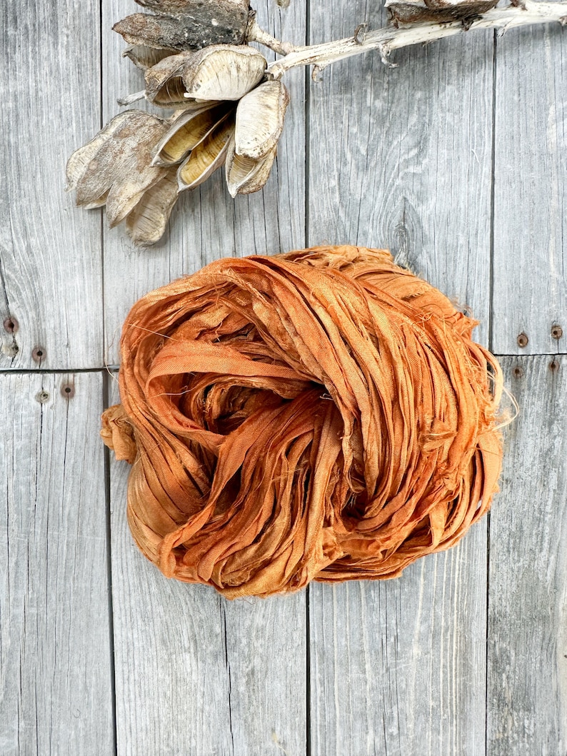 May include: A bundle of orange silk ribbon, loosely tied and arranged on a weathered wooden surface.