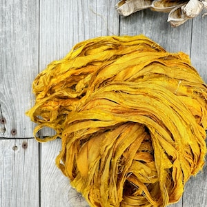 May include: A pile of yellow silk ribbon, with a frayed texture, on a gray wooden surface.