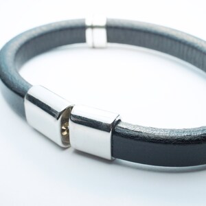 K&ouml;nnte beinhalten: Ein schwarzes Lederarmband mit silbernen Metallschlie&szlig;en. Das Armband ist aus weichem, geschmeidigem Leder gefertigt und hat ein schlichtes, elegantes Design.