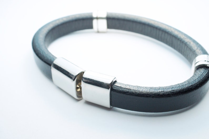 K&ouml;nnte beinhalten: Ein schwarzes Lederarmband mit silbernen Metallschlie&szlig;en. Das Armband ist aus weichem, geschmeidigem Leder gefertigt und hat ein schlichtes, elegantes Design.