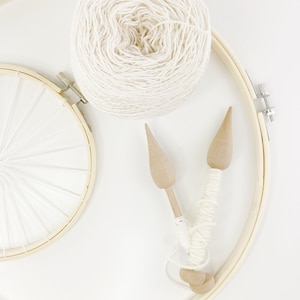 May include: A ball of white yarn, two wooden weaving needles, and a wooden embroidery hoop with white string stretched across it.