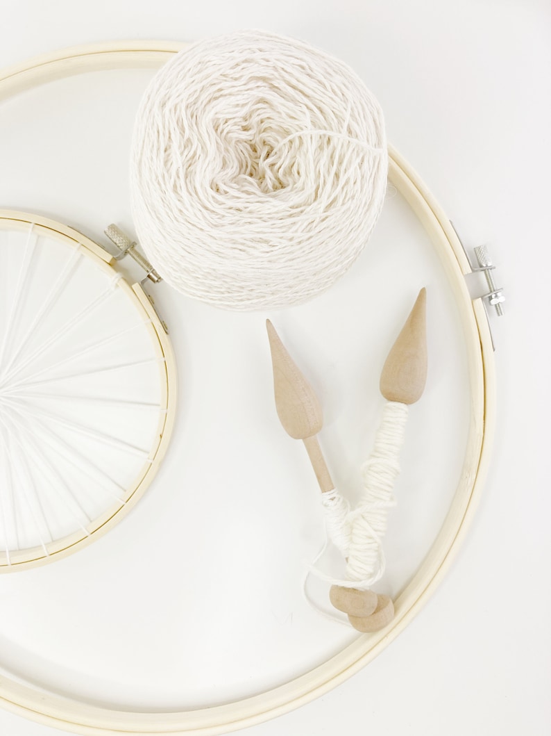May include: A ball of white yarn, two wooden weaving needles, and a wooden embroidery hoop with white string stretched across it.