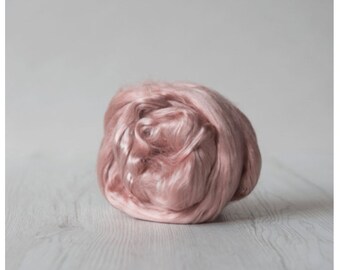May include: A close-up of a ball of soft, pink silk fiber. The fiber is loosely packed and has a slightly iridescent sheen.