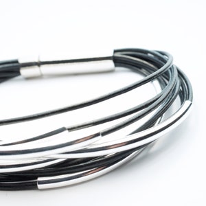 Pulsera de cuero negro de varias vueltas. Tubos de plata de ley. Cierre de acero inoxidable. Estilo rústico.