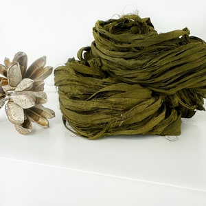May include: A pile of olive green silk ribbon, also known as  silk ribbon yarn, on a white surface.