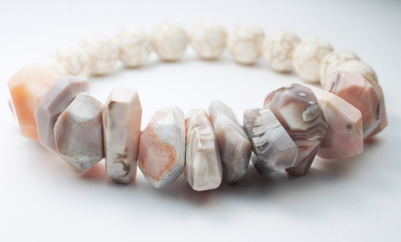 May include: A bracelet made of white and pink agate beads. The beads are faceted and have a natural, organic look.