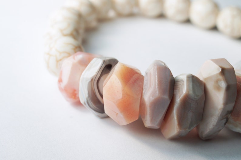May include: A bracelet made of white, pink, and gray gemstone beads. The beads are faceted and have a natural, organic look.