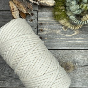 Puede incluir: Primer plano de una cuerda de algodón gruesa de color crema, enrollada sobre una superficie de madera rústica.