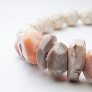 May include: A close-up of a bracelet made of various shades of pink and brown stones. The stones are irregularly shaped and have a natural, polished finish.