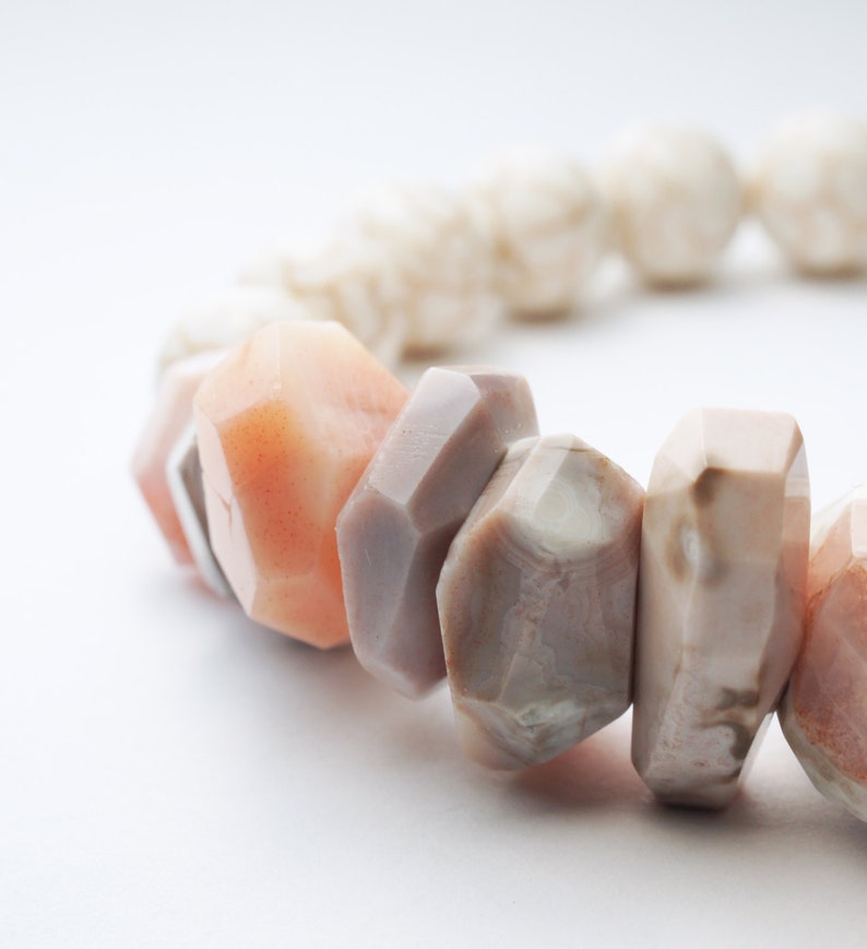 May include: A close-up of a bracelet made of various shades of pink and brown stones. The stones are irregularly shaped and have a natural, polished finish.