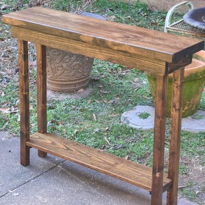 May include: A dark brown wooden console table with a single shelf. The table has a rustic finish and is made of solid wood.