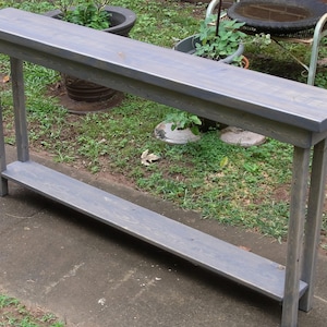 May include: A gray wooden console table with a single shelf. The table has a distressed finish and is made of reclaimed wood.