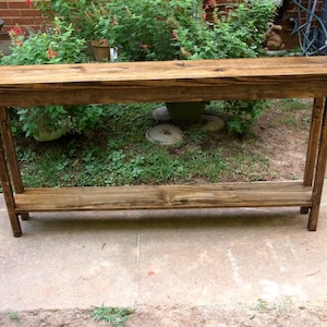 May include: A rustic wooden console table with a natural brown finish. The table has a single shelf and is supported by four legs.