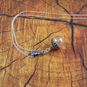 May include: A silver chain necklace with a clear iridescent crystal acorn pendant. The pendant has a silver leaf charm attached to it.