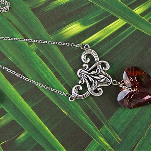 May include: A silver chain necklace with a silver filigree pendant and a dangling heart-shaped crystal. The crystal is a deep burgundy color.