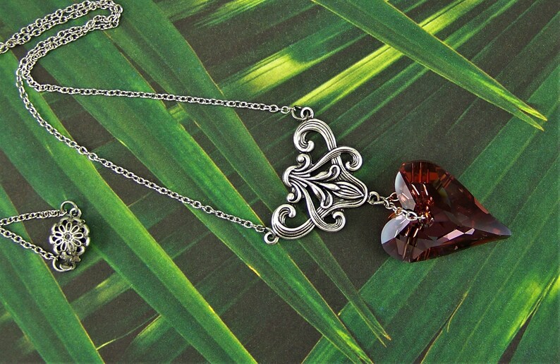 May include: A silver chain necklace with a silver filigree pendant and a dangling heart-shaped crystal. The crystal is a deep burgundy color.