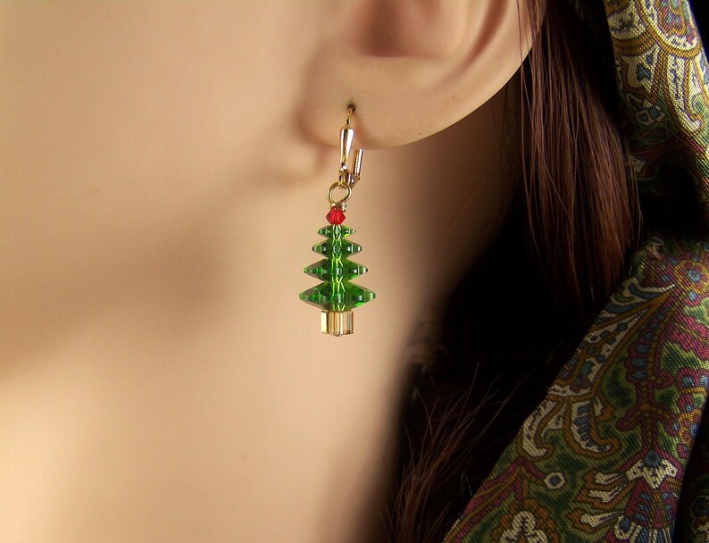 Peut inclure: Une paire de boucles d'oreilles en or avec un motif de sapin de No&euml;l vert et rouge.