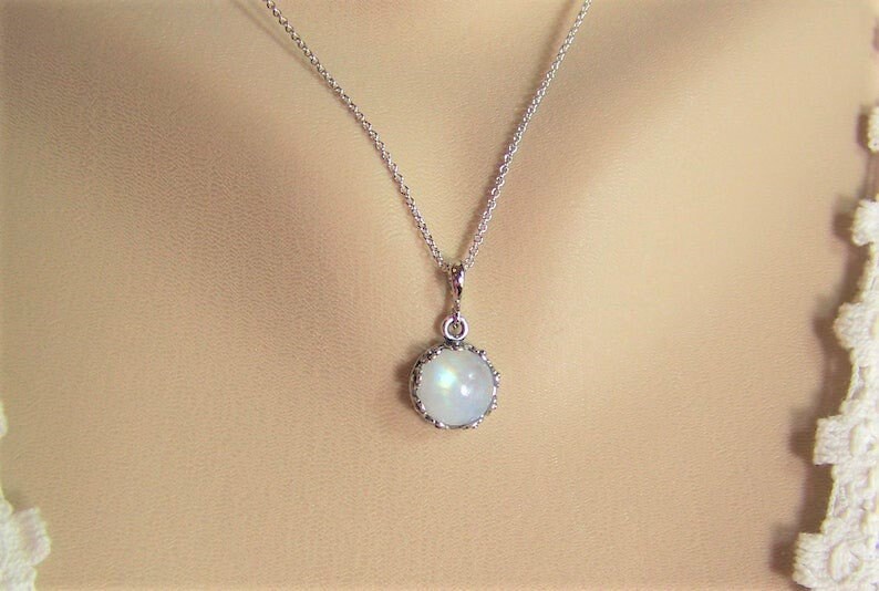 May include: A silver chain necklace with a round, white moonstone pendant set in a silver bezel.