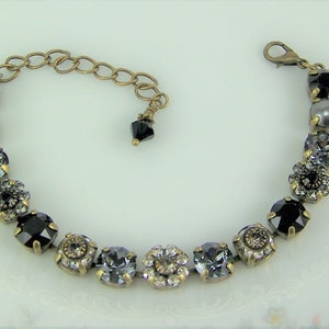 Puede incluir: Una pulsera que presenta una serie de cristales redondos y facetados en negro y gris, montados en engastes de metal color lat&oacute;n antiguo. La pieza incluye una cadena extensora color lat&oacute;n con cierre de mosquet&oacute;n y un peque&ntilde;o dije de cristal negro.