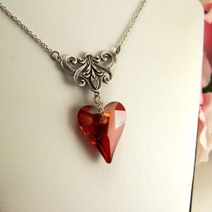 May include: A silver necklace with a delicate filigree design and a dangling red crystal heart pendant.