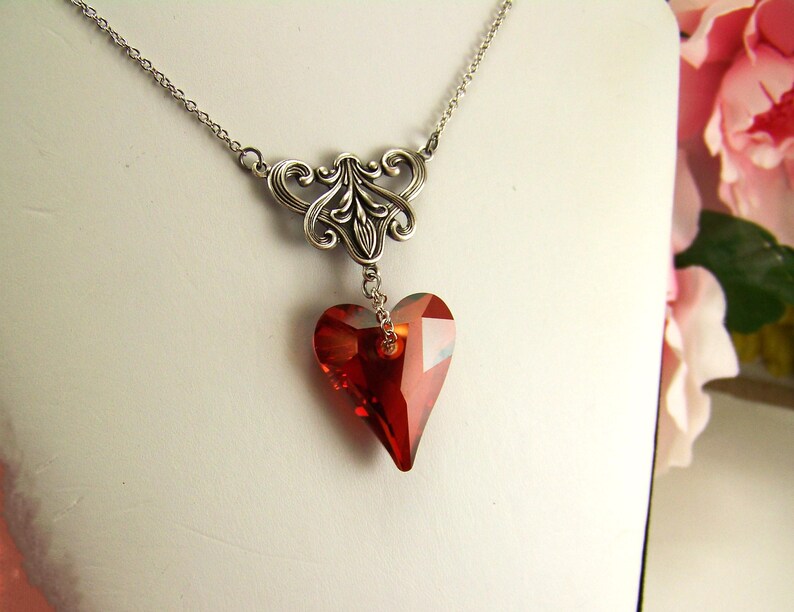 May include: A silver necklace with a delicate filigree design and a dangling red crystal heart pendant.