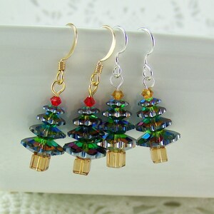 May include: Four Christmas tree earrings with gold, silver, and gold-tone ear wires. Each tree is made of iridescent green and blue crystals, with a red or yellow crystal at the top and a gold-colored base.