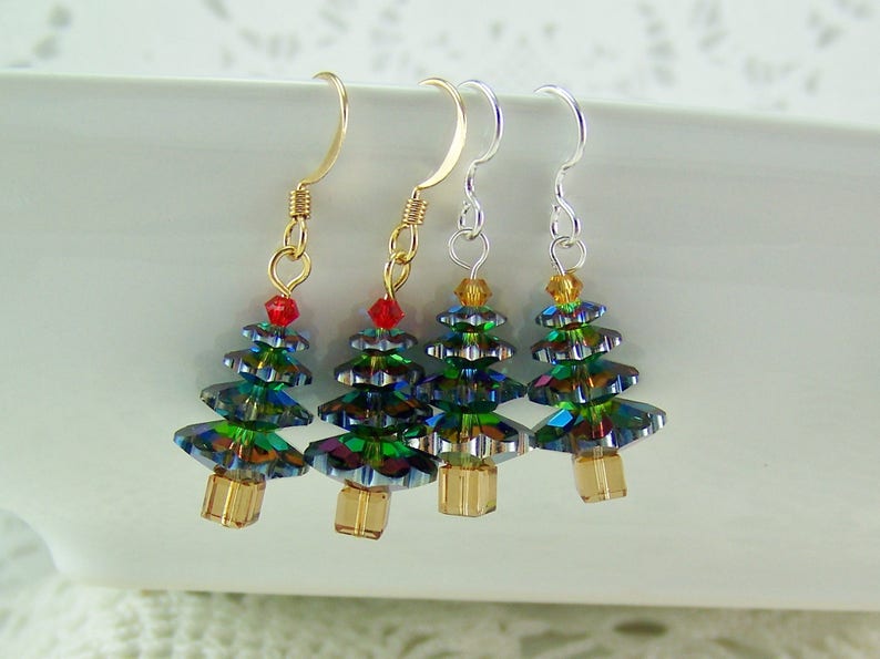 May include: Four Christmas tree earrings with gold, silver, and gold-tone ear wires. Each tree is made of iridescent green and blue crystals, with a red or yellow crystal at the top and a gold-colored base.