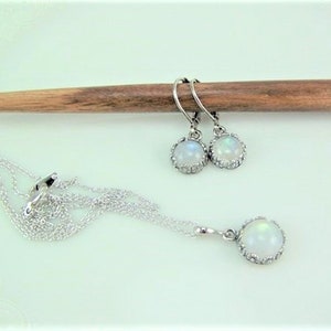 May include: A silver necklace and earrings set with white moonstone pendants. The pendants are surrounded by a silver halo.