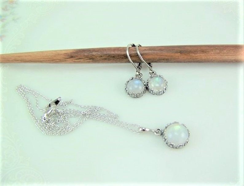 May include: A silver necklace and earrings set with white moonstone pendants. The pendants are surrounded by a silver halo.