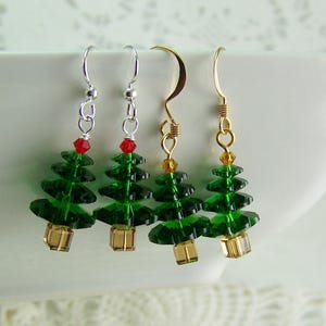 Peut inclure: Trois paires de boucles d'oreilles en forme de sapin de No&euml;l. Les boucles d'oreilles sont faites de perles vertes et dor&eacute;es et pr&eacute;sentent une perle rouge au sommet de chaque sapin. Les boucles d'oreilles sont suspendues &agrave; des crochets argent&eacute;s et dor&eacute;s.