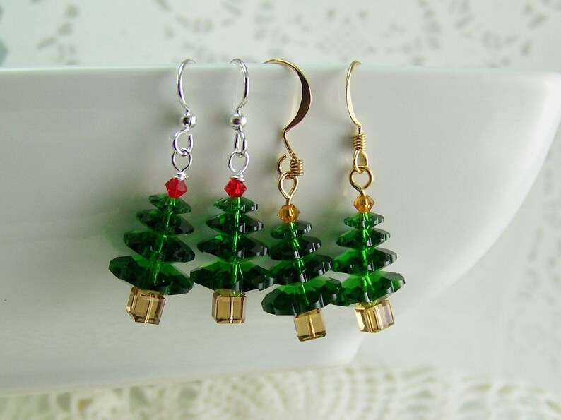 Peut inclure: Trois paires de boucles d'oreilles en forme de sapin de No&euml;l. Les boucles d'oreilles sont faites de perles vertes et dor&eacute;es et pr&eacute;sentent une perle rouge au sommet de chaque sapin. Les boucles d'oreilles sont suspendues &agrave; des crochets argent&eacute;s et dor&eacute;s.