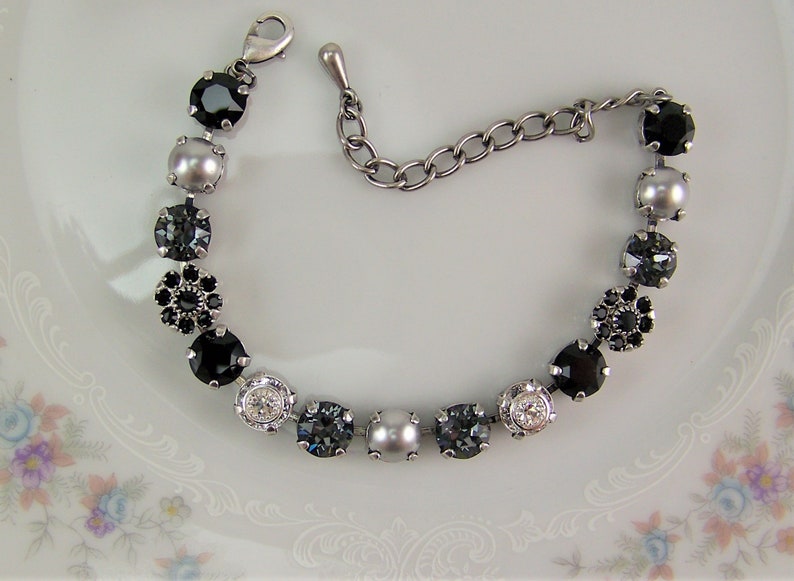 Puede incluir: Una pulsera de tono plateado que presenta una secuencia de cristales negros redondos, perlas grises, piedras facetadas de color gris oscuro y cristales transparentes. Incluye una cadena de extensi&oacute;n met&aacute;lica y un cierre de mosquet&oacute;n.
