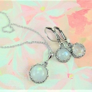 May include: A silver necklace and earrings set with a white moonstone pendant and matching earrings. The stones are set in a silver bezel with a decorative border.