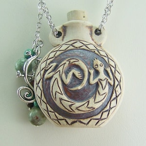 May include: A ceramic pendant necklace with a detailed carving of a lizard on a moon. The pendant is attached to a silver chain with green gemstone beads.