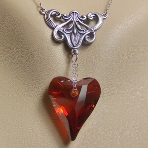 May include: A silver filigree pendant necklace with a dangling red crystal heart.