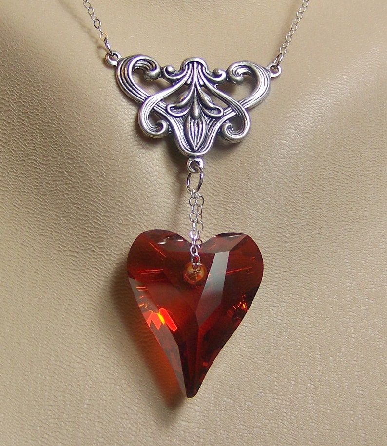 May include: A silver filigree pendant necklace with a dangling red crystal heart.