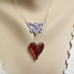 May include: A silver necklace with a delicate filigree design and a dangling red heart-shaped crystal.