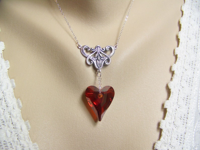 May include: A silver necklace with a delicate filigree design and a dangling red heart-shaped crystal.