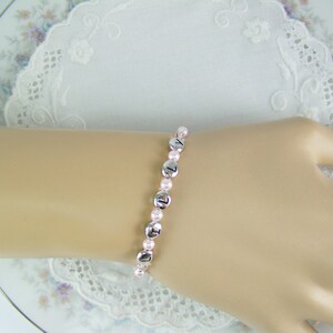 May include: A pink and silver beaded bracelet with silver letter beads spelling out "121".