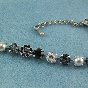 Puede incluir: Una pulsera de tono plateado con una secuencia de cristales negros redondos, perlas grises y piedras facetadas transparentes engastadas en metal. La pulsera incluye una cadena de extensi&oacute;n con un peque&ntilde;o dije en forma de gota y un cierre de mosquet&oacute;n.