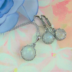 May include: A silver necklace and earrings set with a round, white moonstone pendant and matching earrings. The stones are set in a silver bezel with a decorative border.