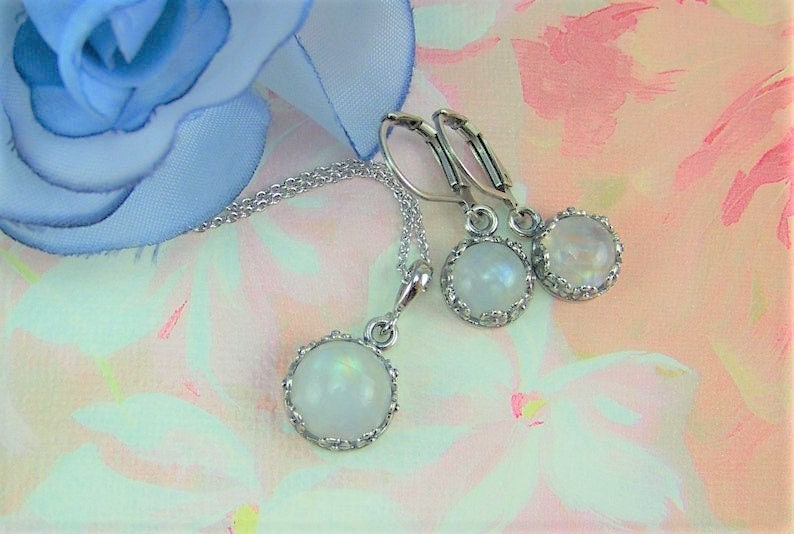 May include: A silver necklace and earrings set with a round, white moonstone pendant and matching earrings. The stones are set in a silver bezel with a decorative border.