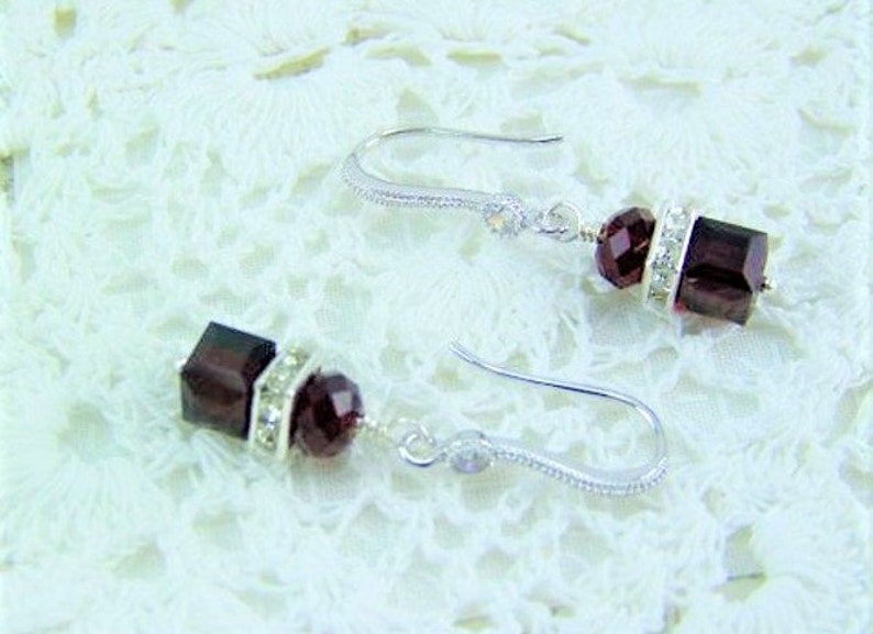 Op de afbeelding: Een paar zilveren oorhangers met een donkerrode vierkante kristal en heldere strass steentjes.